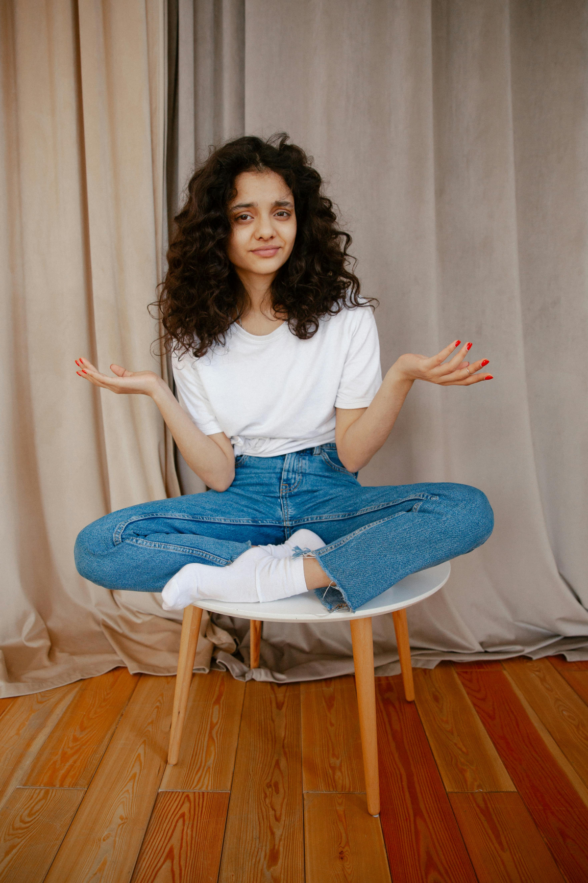 A young woman sits cross-legged on a chair with a questioning expression, symbolising uncertainty in clinical supervision.